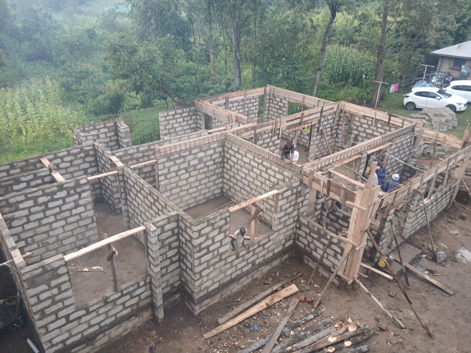 Ground-floor blockwork walls under construction, with ring-beam reinforcement cages and timber column formwork, seen from above